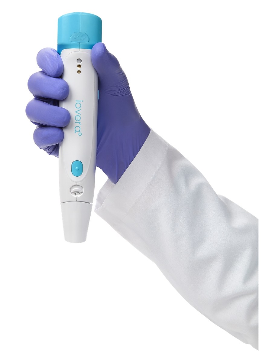 A gloved hand holding the iovera&deg; handheld cryoneurolysis device, showing its size relative to a hand.