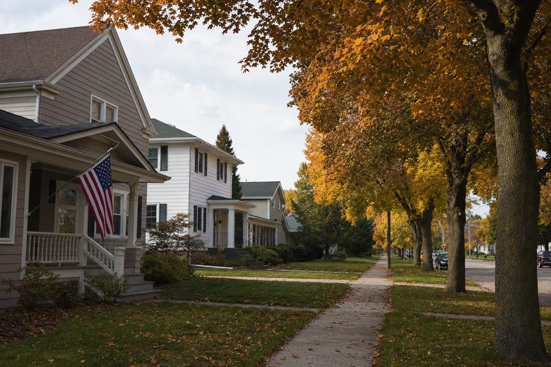 A tree-lined Green Bay residential street with older two-storey homes and maples in full autumn colour.