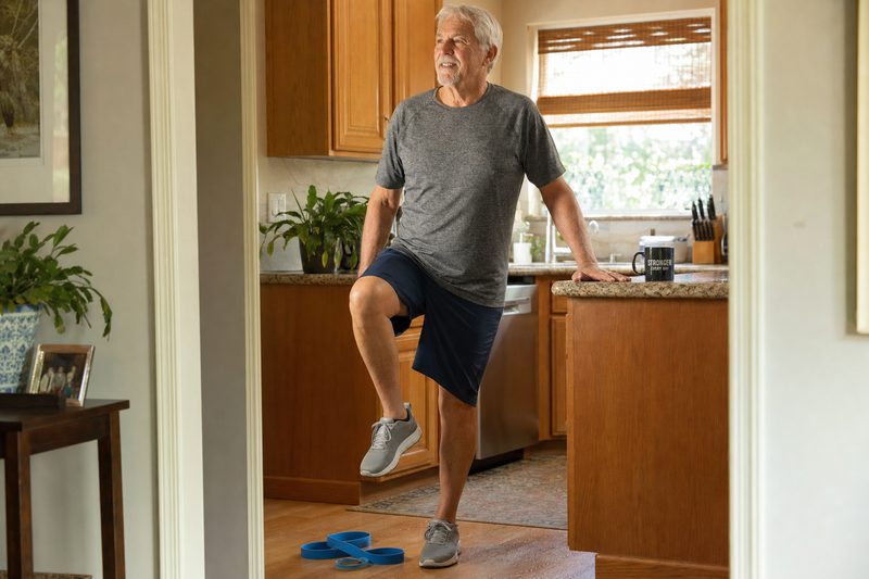 A clinician assessing a seated patient's knee during a visit in the patient's own home.
